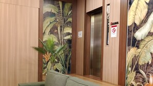 A reception area with a green sofa, wooden panel walls, a plant, and a no-smoking sign. - SH GARDEN HOTEL (Tanah Merah)