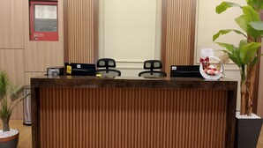 A reception desk with a wooden finish, two black chairs, a potted plant, and a decorative item with flowers. - SH GARDEN HOTEL (Tanah Merah)