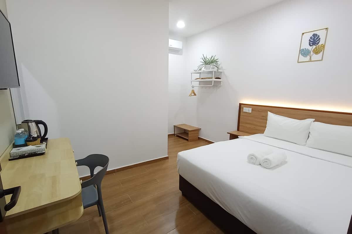 Habitación de hotel con cama, escritorio y silla, una mesita, estantería con plantas y una lámpara de pared.