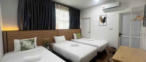 Une chambre d’hôtel avec trois lits, une tête de lit en bois, une table, une chaise, une fenêtre avec des rideaux, un appareil de climatisation et une porte.