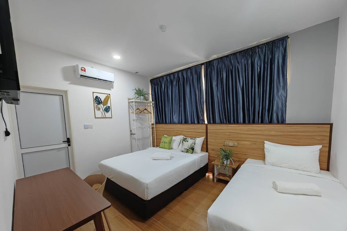 Habitación de hotel con dos camas, un escritorio, aire acondicionado y una ventana con cortinas.