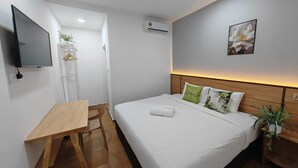 A hotel room with a bed, a desk, a TV, a plant, and a painting on the wall. - SH GARDEN HOTEL (Tanah Merah)