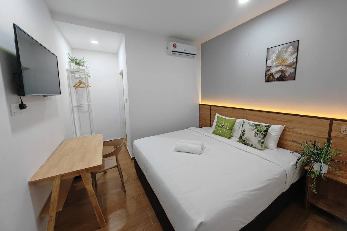 Habitación de hotel con cama, escritorio, televisor, planta y un cuadro en la pared.