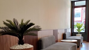 A modern lobby with a seating area, a large potted plant, and a view through a large window. - SH GARDEN HOTEL (Tanah Merah)