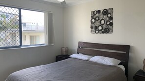 A bedroom with a bed, a window, a wall art piece, and a nightstand.