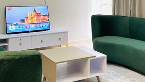 Un salon moderne avec un téléviseur à écran plat, un canapé vert, une table basse et un lustre.