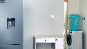 Un espace de vie compact comprenant un réfrigérateur, un lave-linge et un petit bureau.