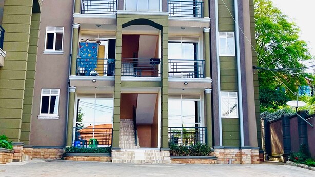 Un immeuble résidentiel à plusieurs étages, doté d’une entrée centrale, de balcons et d’un toit recouvert de tuiles.