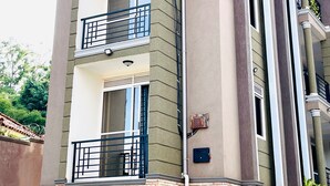 Un immeuble résidentiel à plusieurs étages, doté de balcons, d’un rez-de-chaussée en briques et d’un toit plat.