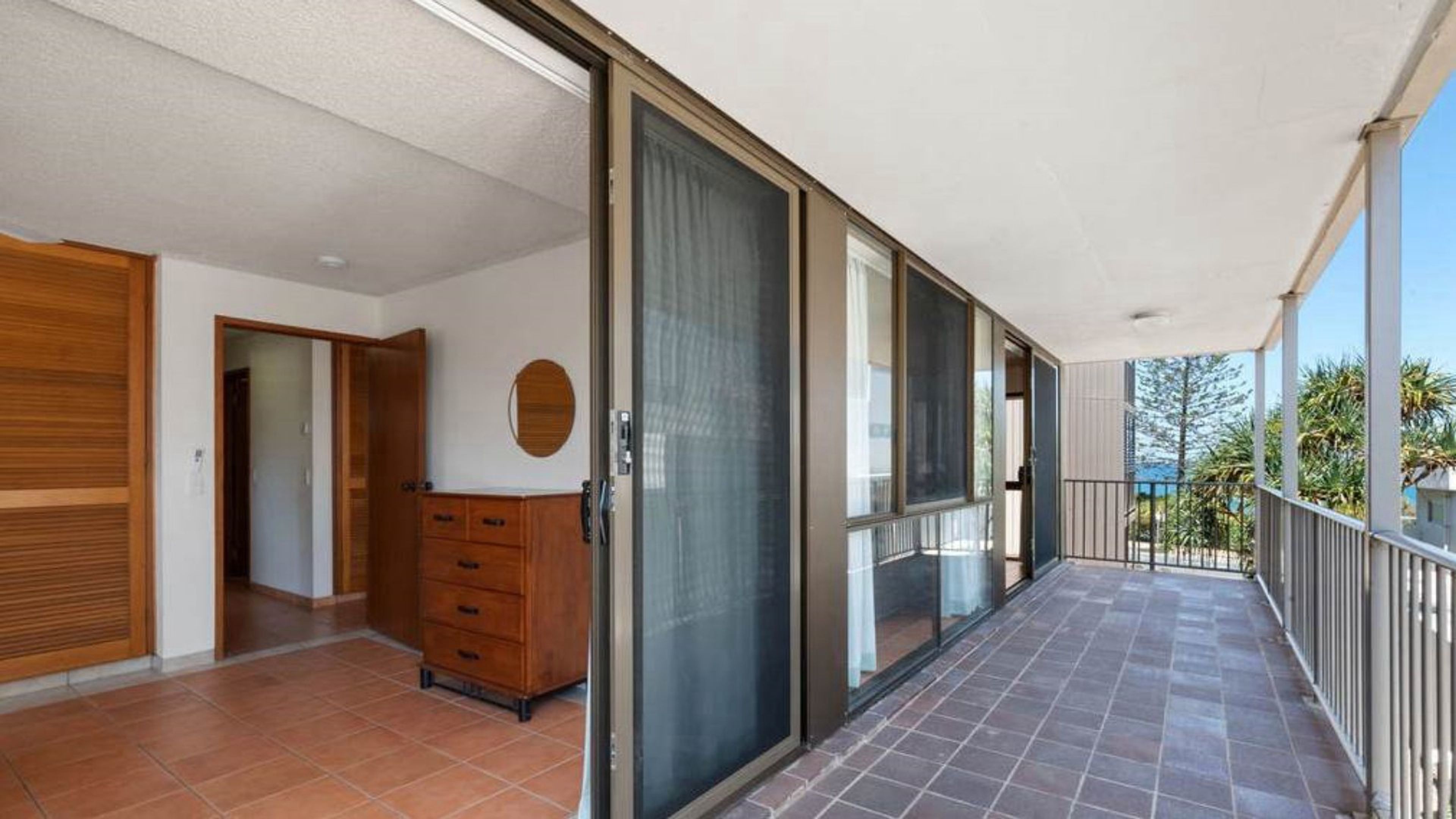 A balcony with a tiled floor, a sliding glass door, and a wooden cabinet.