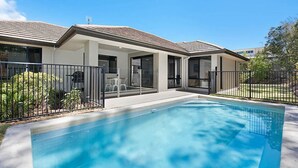 Una casa moderna con piscina, terraza cubierta y jardín cercado.