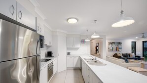 Una cocina moderna con electrodomésticos de acero inoxidable, armarios blancos, una isla central con pileta e iluminación colgante.
