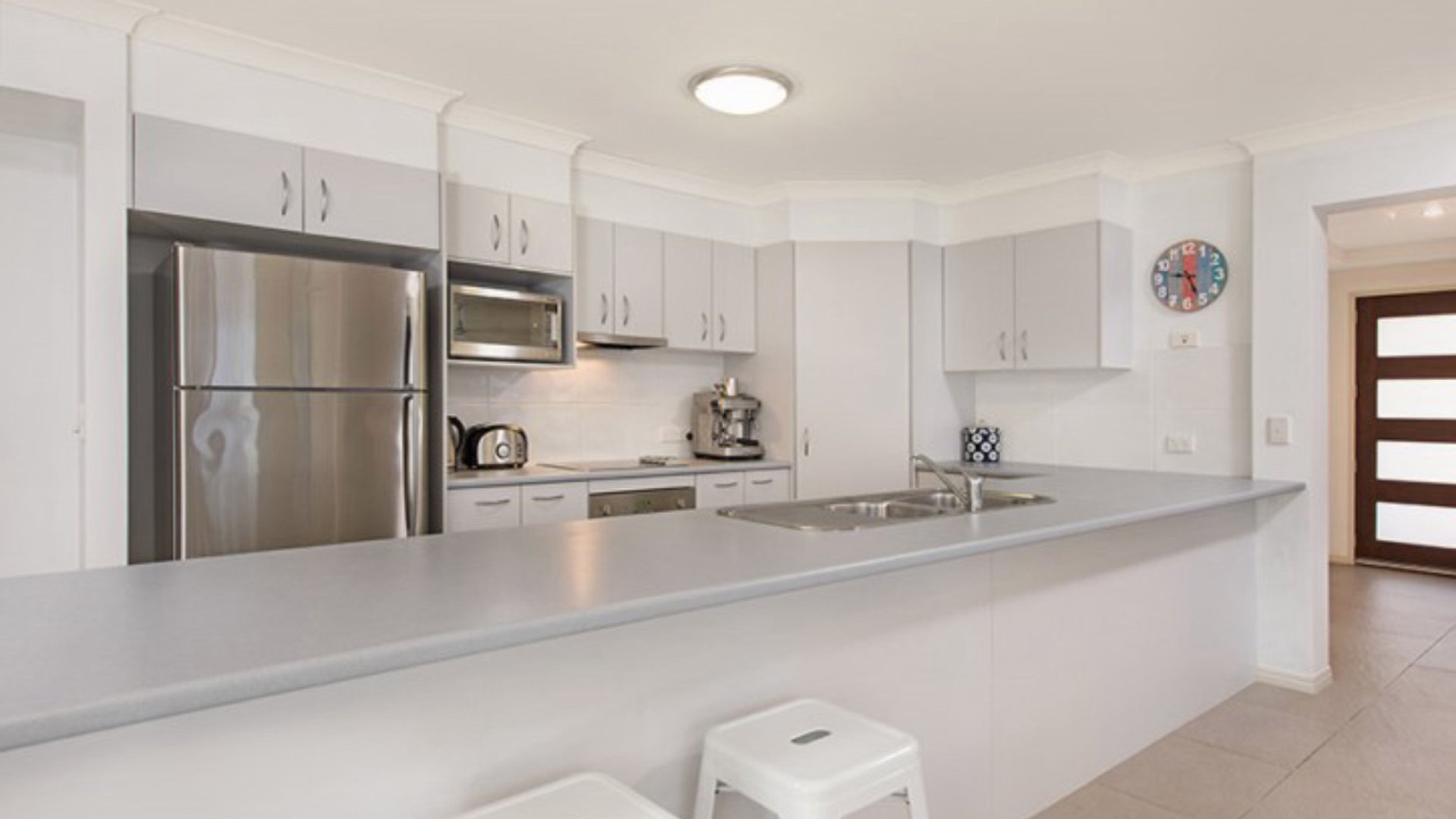 Una cucina moderna con elettrodomestici in acciaio inossidabile, mobili bianchi e un'isola centrale con sgabelli.