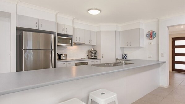 Una cocina moderna con electrodomésticos de acero inoxidable, muebles blancos y una isla central con taburetes.