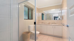 A modern bathroom with a glass shower enclosure, a toilet, a sink with a mirror above, and a cabinet. - 4BR Pool Hideaway Near Beach (Moffat Beach)