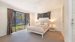 A bedroom with a large window, a bed, a nightstand, and a ceiling fan. - 4BR Pool Hideaway Near Beach (Moffat Beach)