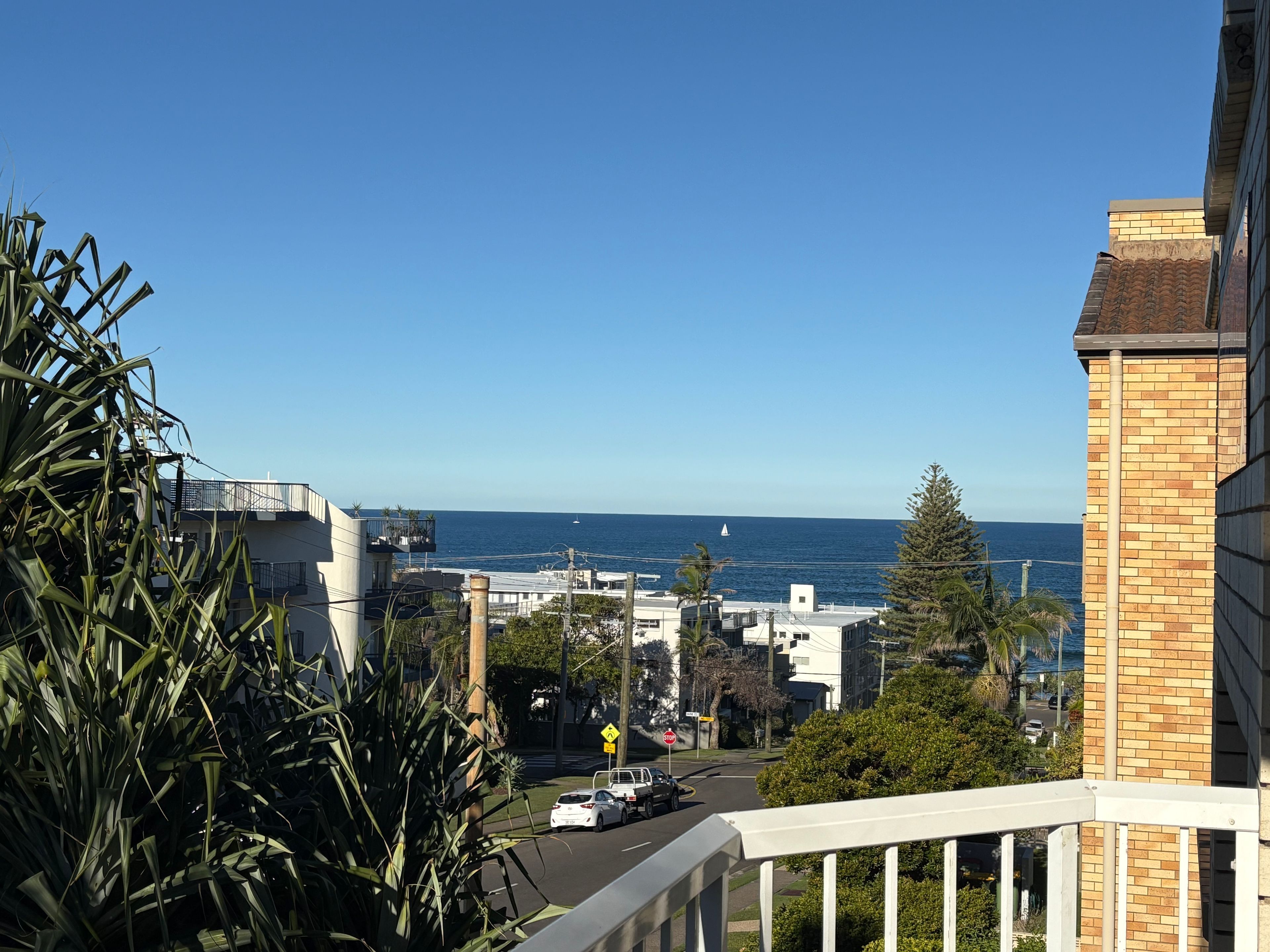 Une vue sur la côte depuis un balcon, avec un ciel dégagé, une route où circulent des véhicules et un panneau de signalisation indiquant un arrêt.