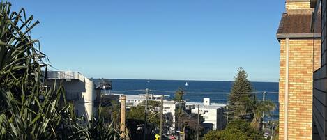A coastal view from a balcony with a clear sky, a road with vehicles, and a stop sign.