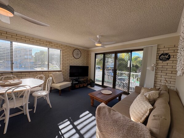 A living room with a TV, seating, a coffee table, and a balcony with a view. - Whiteopal Close To Kings Beach With Ocean Views (Kings Beach)