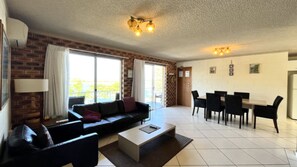 Een woonkamer met een bank, salontafel en een eethoek met stoelen.