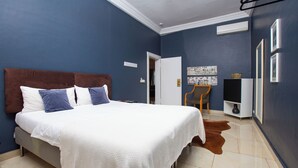 A bedroom with a large bed, a chair, a television, and a door leading to another room.
