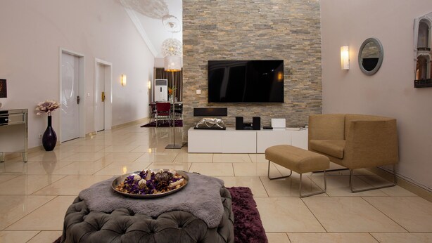 A modern living room with a stone wall, a flat-screen TV, a sofa, and a decorative table with flowers.