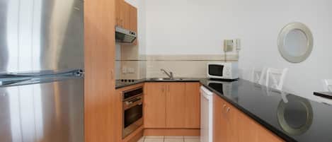 A compact kitchen with a stainless steel refrigerator, a microwave, and wooden cabinets.