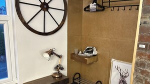 Una habitación acogedora con una gran rueda de madera, un escritorio con lámpara, una silla, un perchero y un cuadro de un ciervo.