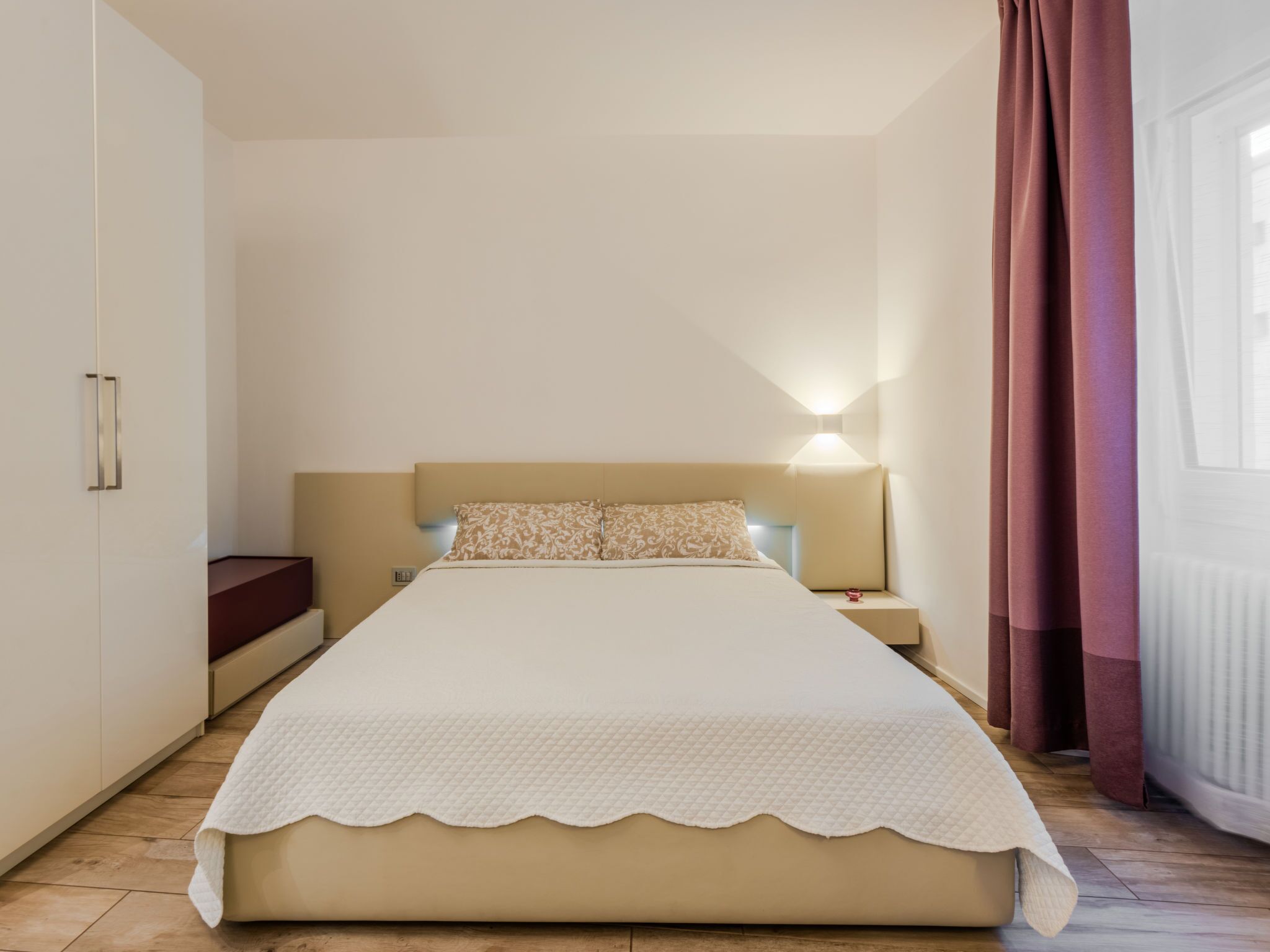 Ein Schlafzimmer mit einem großen Bett, einem Nachttisch, einem Kleiderschrank und einem Fenster mit Vorhängen.