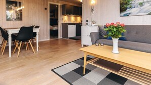 A cozy living room with a dining area, wooden walls, a painting of a waterfall, and a vase with flowers on a table. - 6 Person Holiday Home in Otterup (Otterup)