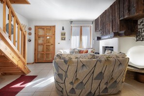 A room with a wooden staircase, a sofa with a leaf pattern, a fireplace, and a wooden wall with decorations.