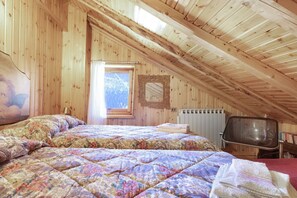 A wooden-paneled attic bedroom with a bed, a television, and a window with a view.