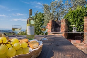 A wooden table with a bottle of white wine, two glasses, a basket of grapes, and a brick oven. - Chianti Apt Olmo&Pini Shared Pool, Castelfiorentino, Italy (Castelfiorentino)