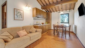 A cozy living room with a sofa and a dining table with chairs. There is a kitchen area with wooden cabinets and a tiled backsplash. - Chianti Olmo&Pini Shared Pool, Castelfiorentino, Italy (Castelfiorentino)