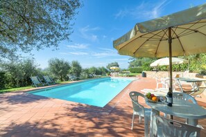 A swimming pool with lounge chairs and a table with fruit and a bottle.