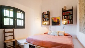 Un dormitorio con una cama, una silla, una estantería y una ventana.