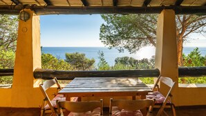 Mesa y sillas de madera al aire libre bajo una pérgola, con vista al mar.