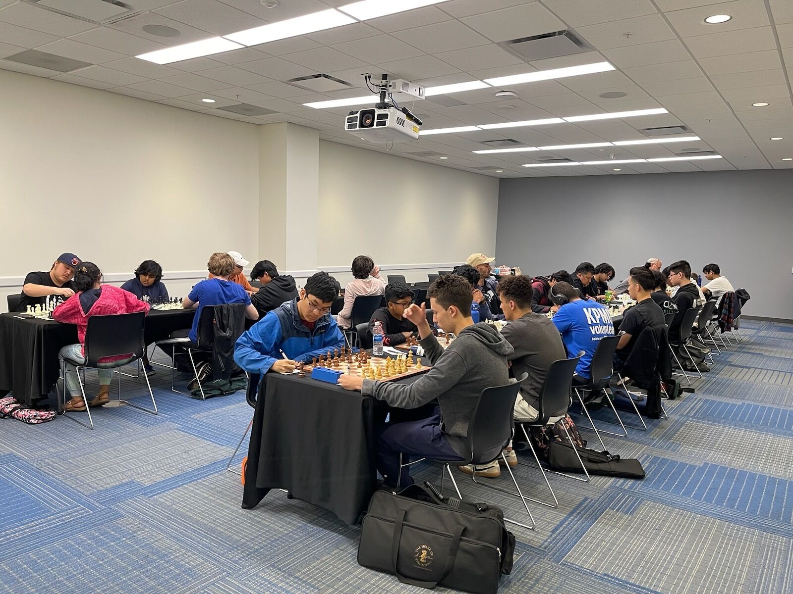 Une salle de conférence avec plusieurs tables disposées en rangées, équipées de jeux d’échecs, ce qui laisse supposer qu’un tournoi ou un événement d’échecs y est organisé.