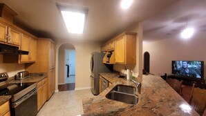 A kitchen with wooden cabinets, a stainless steel refrigerator, granite countertops, a built-in oven, a sink, and a television on the wall. - Nice House in One of the Best Neighborhood in Tallahassee (Tallahassee)