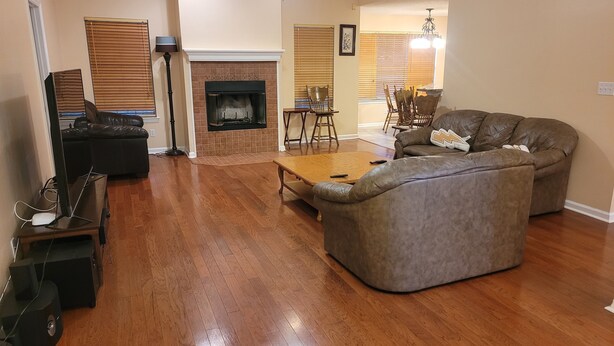 A living room with a fireplace, leather sofa, wooden coffee table, and a dining area with chairs and a chandelier. - Nice House in One of the Best Neighborhood in Tallahassee (Tallahassee)