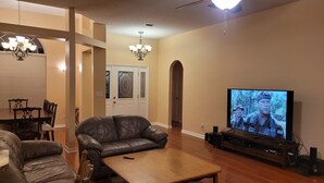 A living room with a leather sofa, wooden coffee table, and a television displaying a movie. - Nice House in One of the Best Neighborhood in Tallahassee (Tallahassee)