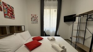 A hotel room with a bed, red pillows, rolled towels, a TV, and a wardrobe. - Arsenale Suites, Family Comfort. Perfect for families or friends to relax (Torino)