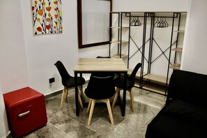 A small room with a wooden table, black chairs, a red storage unit, and a metal shelving unit with clothes hanging.