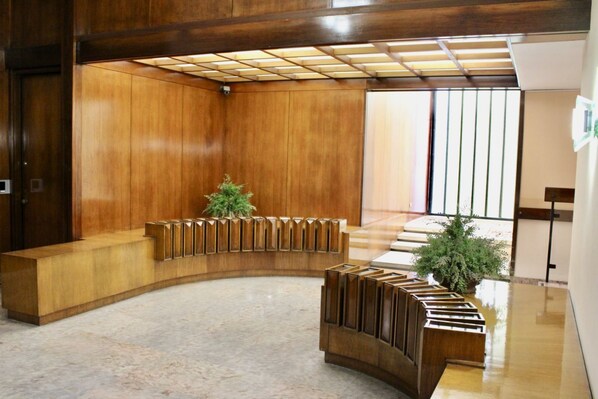 Un espace d’accueil avec un bureau en bois aux lignes courbes, une plante en pot et un escalier en arrière-plan.