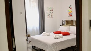 A hotel room with a bed, white linens, a red pillow, a wall art piece, and a window with curtains. - Arsenale Suites, Love Nest. A cozy retreat for two, where romance meets comfort (Torino)