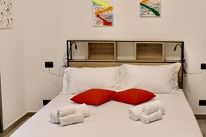 Een net opgemaakt bed met witte en rode kussens, een houten hoofdbord en twee kunstwerken aan de muur.