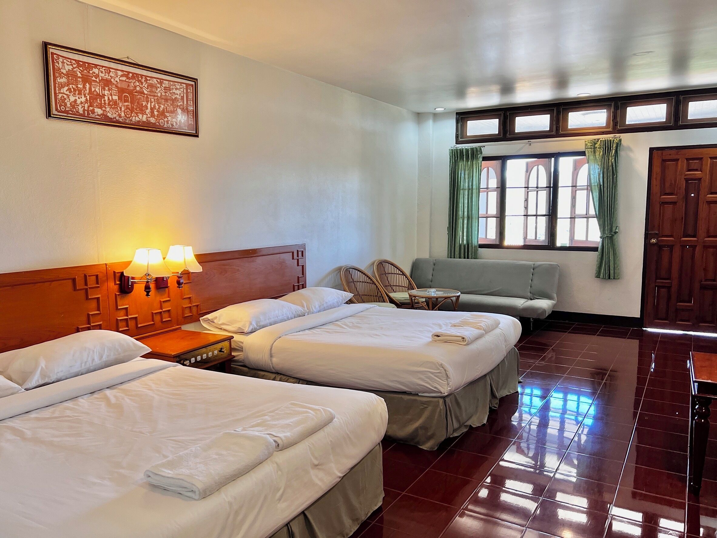 A hotel room with three beds, a wooden headboard, a wall-mounted picture, a window with curtains, and a wooden door.