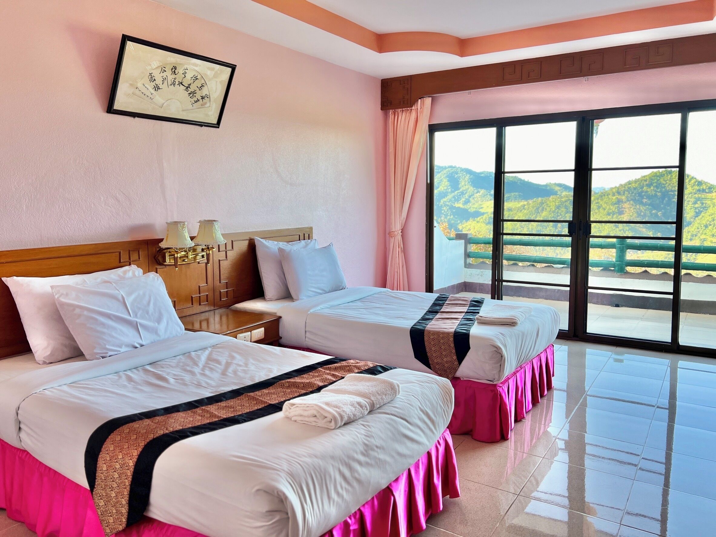A hotel room with two beds, a large window with a view of greenery, and a framed certificate on the wall.