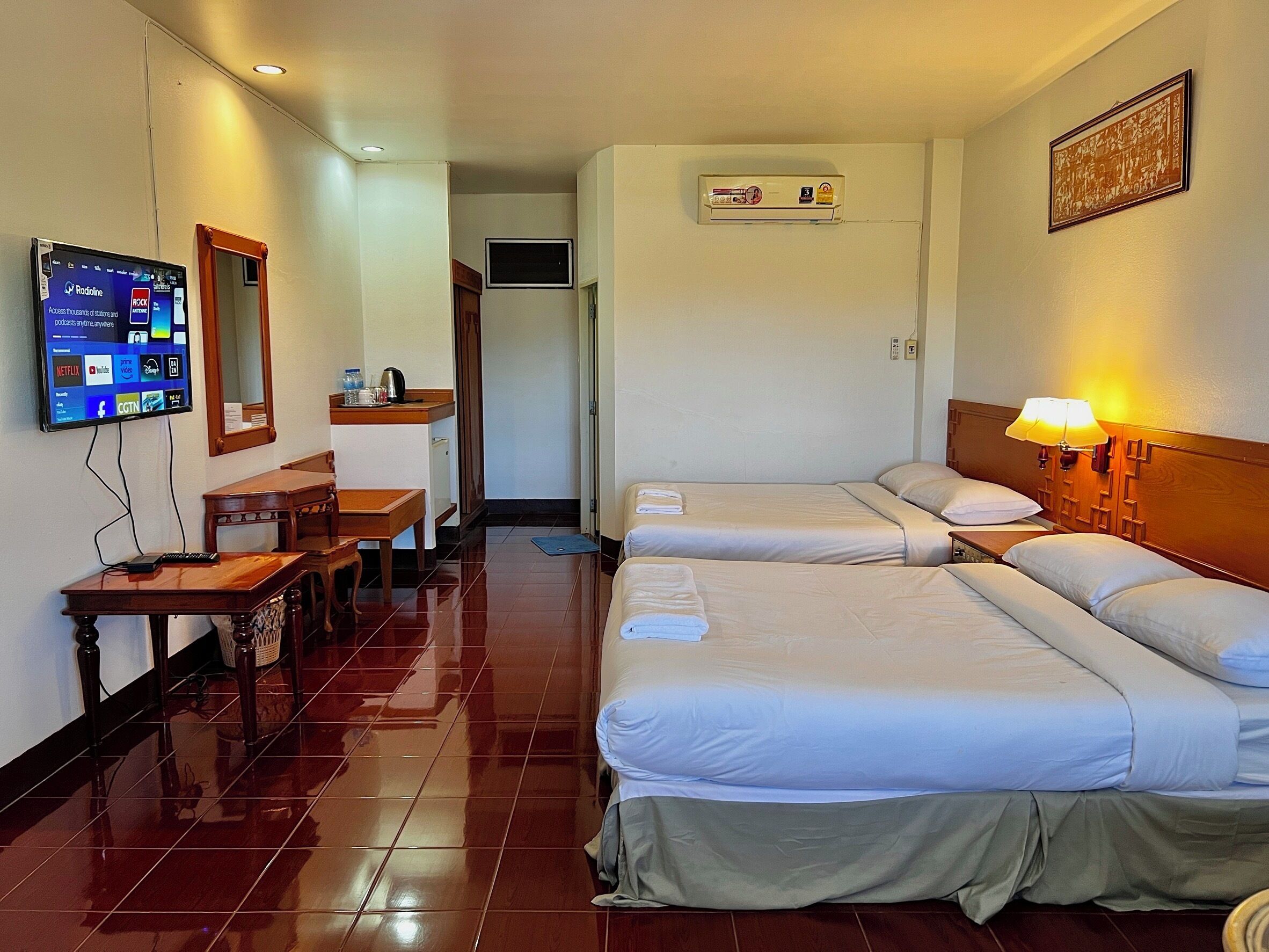 A hotel room with two beds, a desk, a chair, a TV mounted on the wall, and an air conditioning unit.