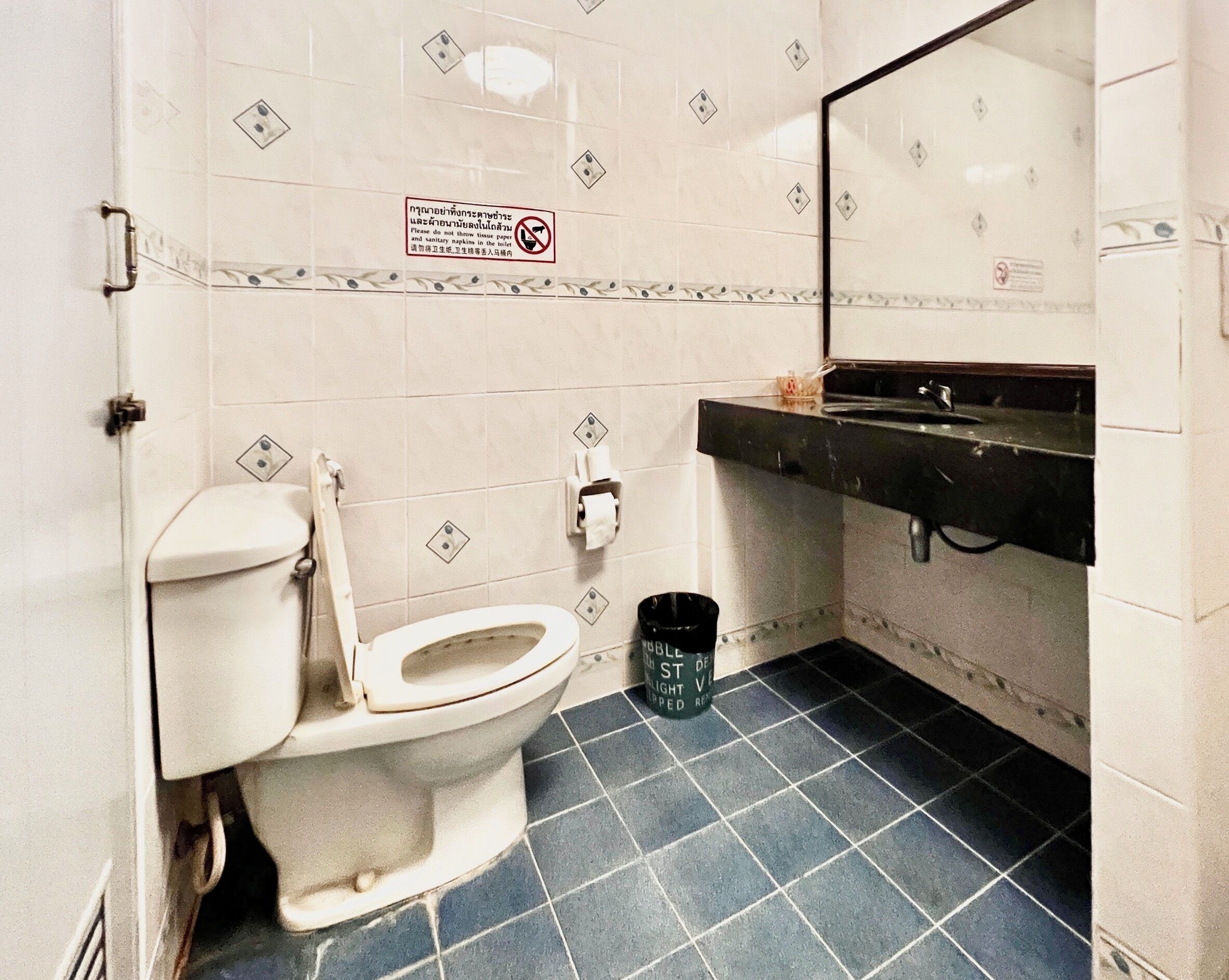 Un baño con inodoro, lavamanos y un cubo de basura.